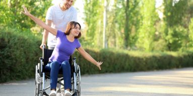 Young woman on a wheelchair with her partner having fun outdoors — Disability Support Services in Maitland, NSW