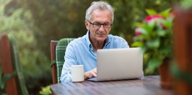 Elderly man going through his laptop while having coffee outdoors — Disability Support Services in Gawler, SA