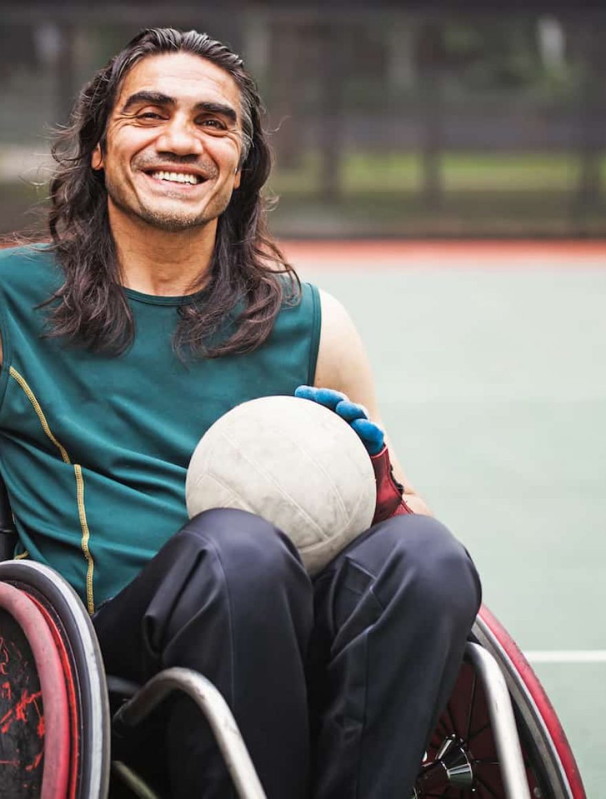 Guy on a wheelchair holding a white volleyball — Disability Support Services in Robina, QLD